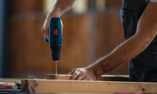 Person using a cordless drill on a wooden surface with a blurred background